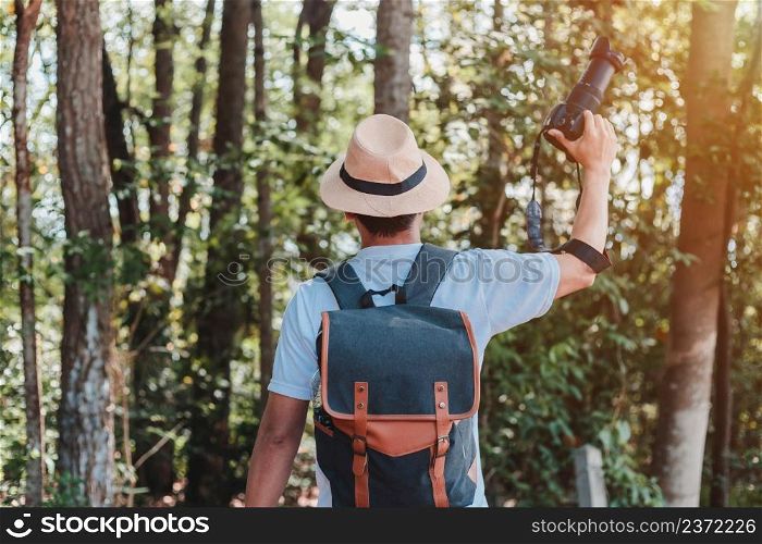 A male tourist carrying a handbag, water bottle and camera walks through the forest.