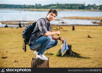 A male traveler with a backpack carrying a map and sitting on a tree stump.