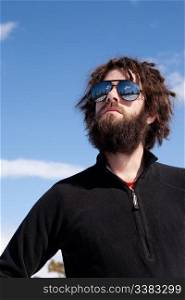 A male with a full beard and retro sunglasses standing in a winter landscape ready for adventure