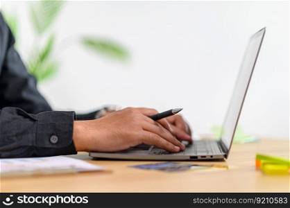 A male worker using a laptop with a pen clip in his hand. Selective focus