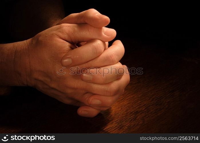 A man&acute;s hands folded in prayer with very dramatic lighting