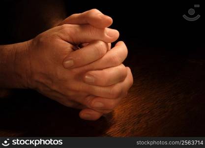 A man&acute;s hands folded in prayer with very dramatic lighting