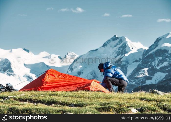 A man adventurer sets up his tent in the high mountains
