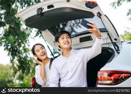 A man and a woman sit happily in the trunk of a car and take a selfie on the phone.