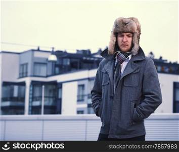 A man and wearing a fur hat and warm overcoat, apartment buildings on background
