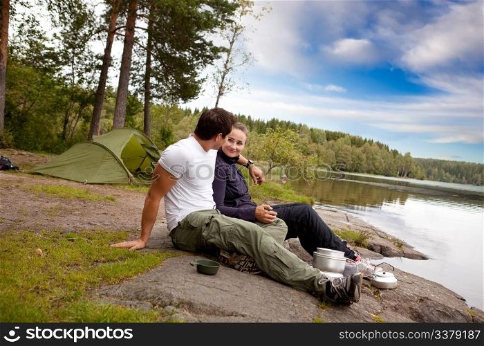 A man and woman happy camping in the forest by a lake