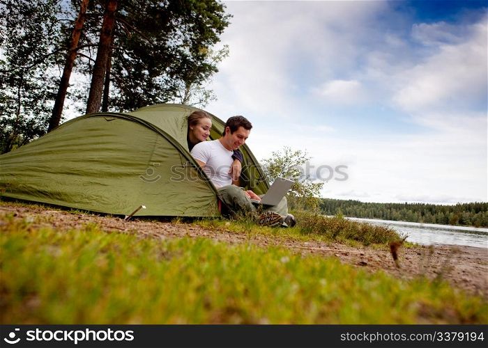 A man and woman using a computer outdoors in a tent
