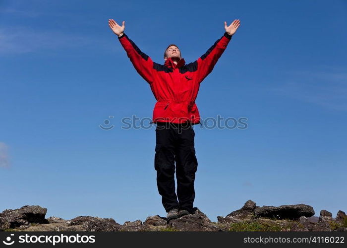 A man arms outstretched celebrating success at the top of a mountain.