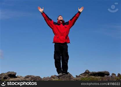 A man arms outstretched celebrating success at the top of a mountain.