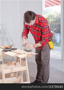 A man at home using an electric hand sander with safety goggles
