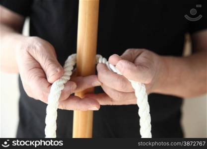 A man begins to tie a thick rope around a wooden pole.