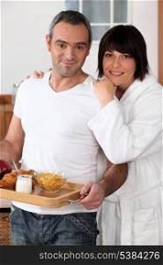 a man bringing breakfast on a platter and his wife wearing a bathrobe