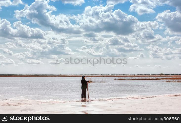 A man by the lake among the reeds in a quartz sand quarry with a distant horizon and a beautiful cloudy sky.. Man By The Lake Among Quartz Sand Under Beautiful Cloudy Sky