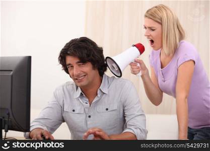 a man doing computer and a woman yelling on him with a megaphone