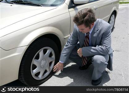A man dressed for a business meeting discovering a flat tire on his car.