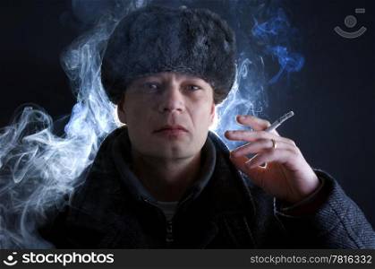 A man, dressed in Soviet attire, smoking a cigarette, surrounded by smoke.