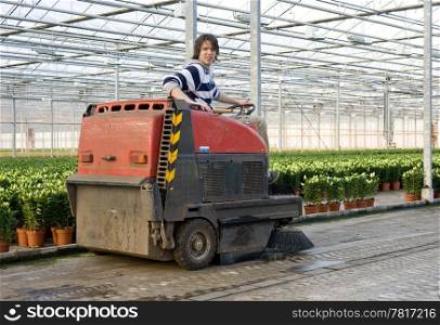 A man, driving an industrial cleaning cart, working hiw way through the concrete flooring of a huge glasshouse