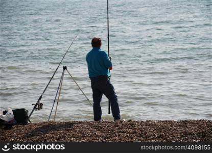 A man fishing in the sea from the beach at Sandgate in Kent, England