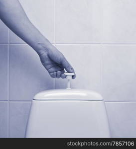 A man flushing the toilet, glazed tiles on background, blue tinted image