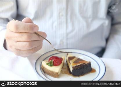 a man getting ready to eat two different kinds of cheesecake - a plain one topped with a fresh strawberry and a chocolate one with a caramel sauce