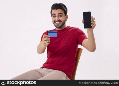 A MAN HAPPILY SHOWING MOBILE PHONE AND DEBIT CARD IN FRONT OF CAMERA