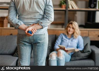 A man holds a box with a ring behind his back and preparing to make a wedding proposal. Love couple in living room together. Happy lifestyle, beautiful relationship