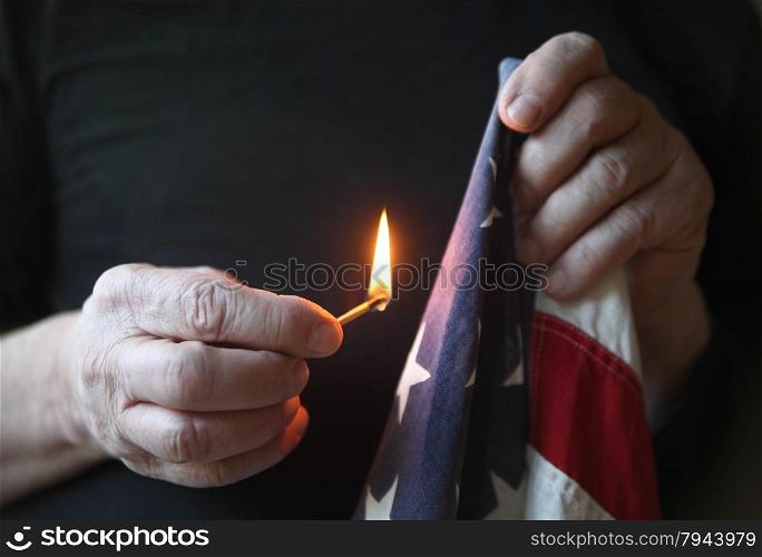 A man holds a match up to an old USA flag.
