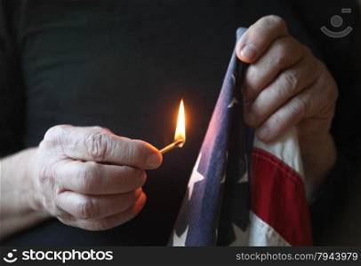 A man holds a match up to an old USA flag.