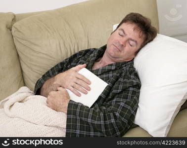 A man home sick from work has fallen asleep while reading.