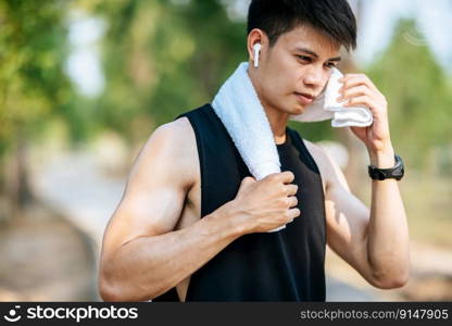 A man in a black shirt stood and held a handkerchief over his neck to wipe his face after exercising.