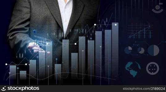 a man in a black suit holds a miniature cart against the background of a holographic graph with increasing indicators. Growth in business sales, high margins. Big profit