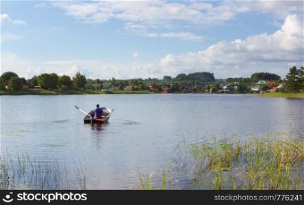 A man in a boat rowing to the village houses on a distant shore at sunny summer day. The concept of tourism, vacation, hobbies and outdoor activities - space for copy, selective focus. Lake Seliger, Russia.
