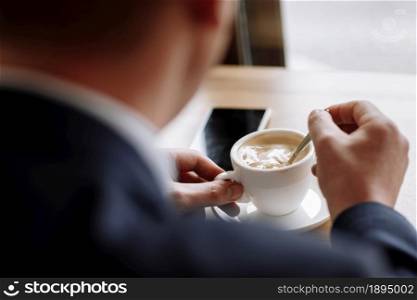 A man in a business suit holds a cup of hot coffee in his hands. Morning businessman in cafe .Copy space. A man in a business suit holds a cup of hot coffee in his hands. Morning businessman in cafe .Copy space.
