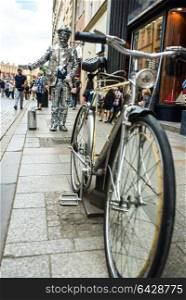 a man in a mirror suit with a suitcase and a bicycle is calling to the Krakow store