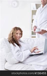 A man in a robe brings coffee girl with laptop