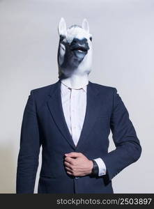 A man in a suit and a horse mask on a light background. Conceptual business background. man with a horse mask on a light background