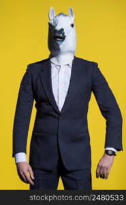 A man in a suit and a horse mask on a yellow background. Conceptual business background. man with horse mask on yellow background