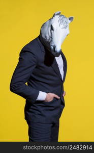 A man in a suit and a horse mask on a yellow background. Conceptual business background. man with horse mask on yellow background