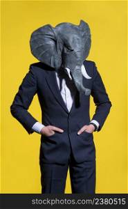 A man in a suit and an elephant mask on a yellow background. Conceptual business background. man with an elephant mask on a yellow background