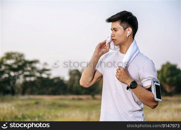 A man in a white shirt stood and held a handkerchief over his neck to wipe his face after exercising.