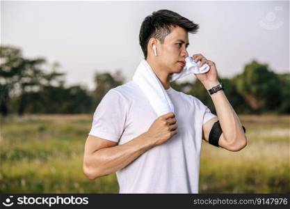 A man in a white shirt stood and held a handkerchief over his neck to wipe his face after exercising.