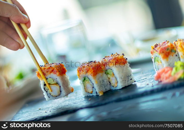 A man in an asian restaurant, eating sushi with chopsticks, trendy oriental food, traditional Japanese cuisine