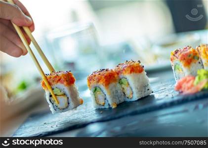 A man in an asian restaurant, eating sushi with chopsticks, trendy oriental food, traditional Japanese cuisine
