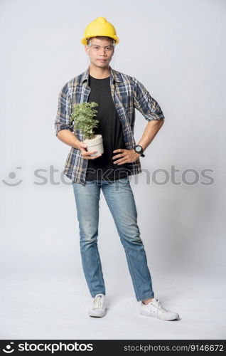 A man in an engineering hat and stood holding a plant pot in his house.