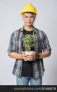 A man in an engineering hat and stood holding a plant pot in his house.