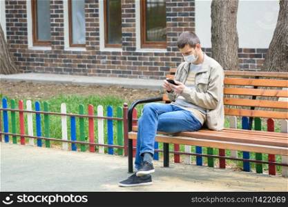 A man in the isolation mode walks on the street and crouches on a bench, looks at the phone screen