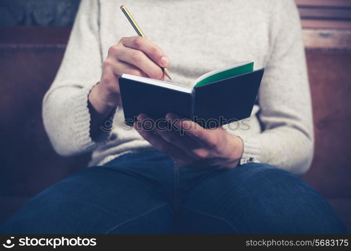 A man is sitting on a sofa and writing notes in a notebook