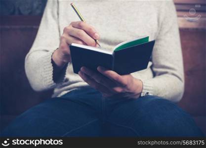 A man is sitting on a sofa and writing notes in a notebook