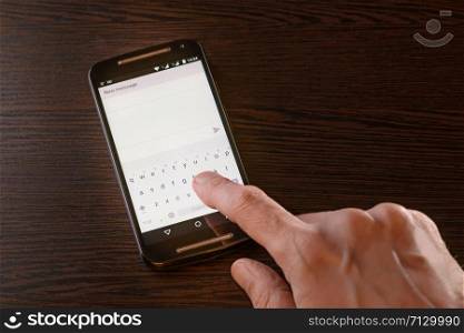 A man is typing an sms on the keypad of his black smartphone