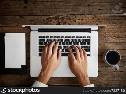 A man is typing on laptop keyboard on modern white office desk, top view. A man is typing on laptop keyboard on modern white office desk